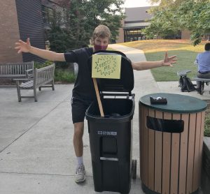 Student wrapping arms around "Feed me" sign on bin