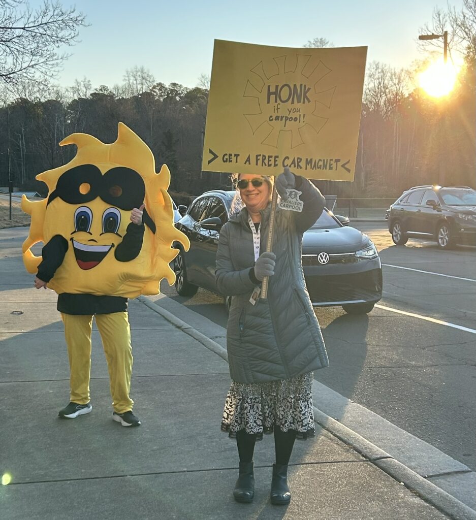 Sun mascot and teacher with sign: "Honk if you carpooled today"